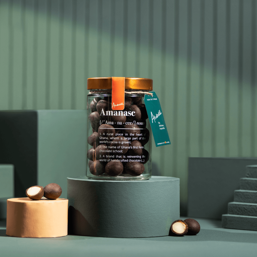 Amanase Bio-Macadamia im Glas, links und rechts eine Macadamia-Hälfte und eine ganze
