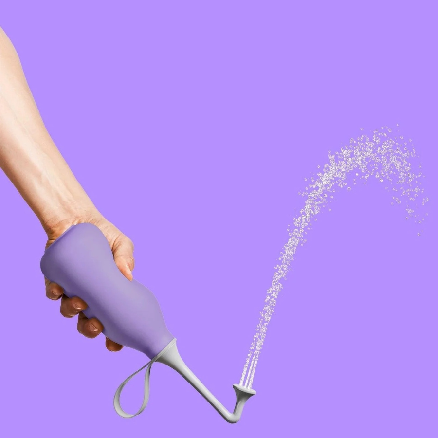 Eine Hand spritzt Wasser aus der Po- und Intimdusche von Bidetlity – Proud Purple