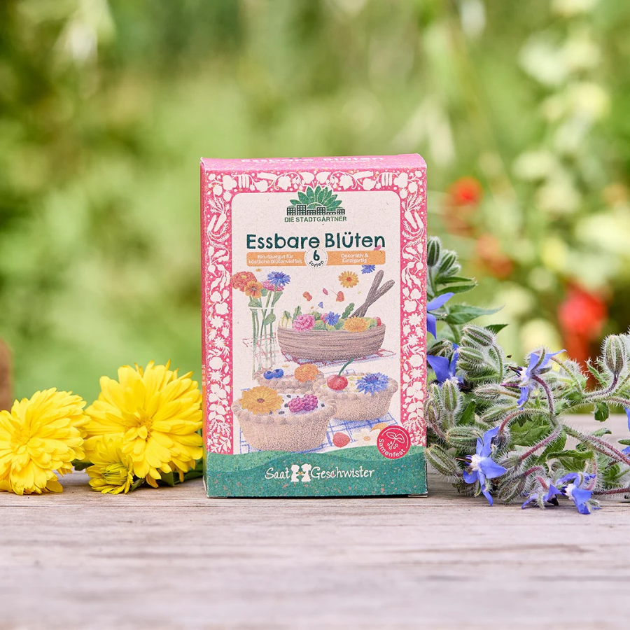 Saatgut-Set Essbare Blüten von Die Stadtgärtner – Verpackung, im Hintergrund Blüten