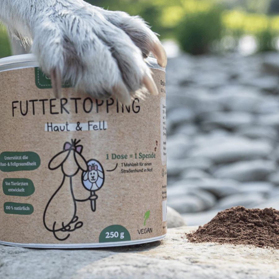 Futtertopping Haut & Fell von Hunderunde. Dose steht auf einem Stein. Hundepfote liegt darauf