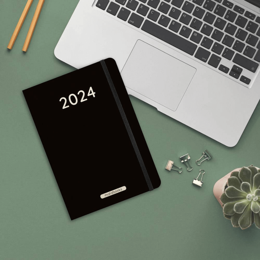 Matabooks Samaya Jahresplaner 2024 "Black" liegt auf einem Tisch neben einem Laptop