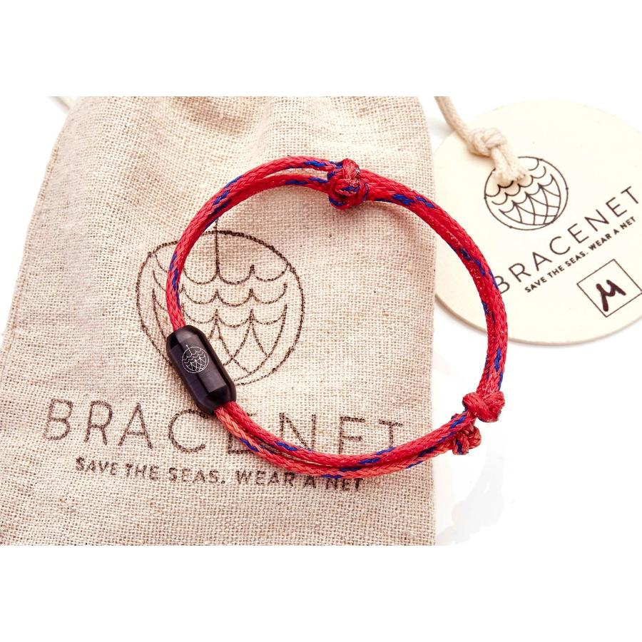 Rotes Armband von Bracenet aus geborgenen Fischernetzen mit Knoten und schwarzem Verschluss auf Verpackungsbeutel liegend