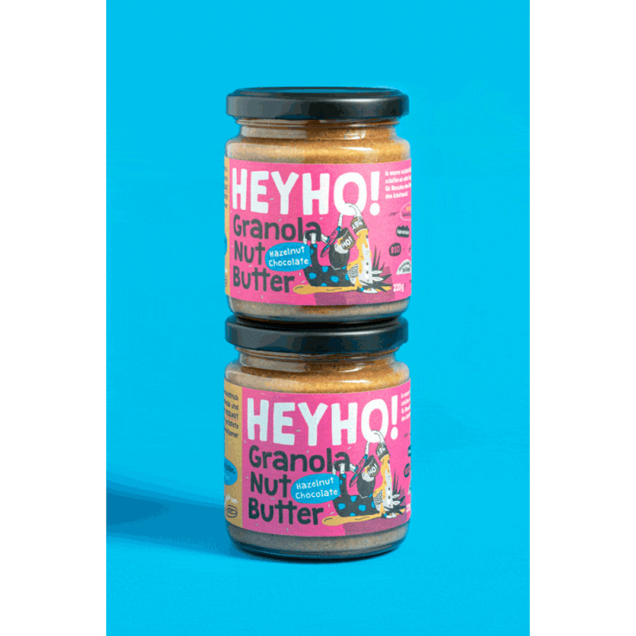 Zwei Gläser Heyho Granola Nussbutter Hazelnut Chocolate stehen übereinander vor blauem Hintergrund