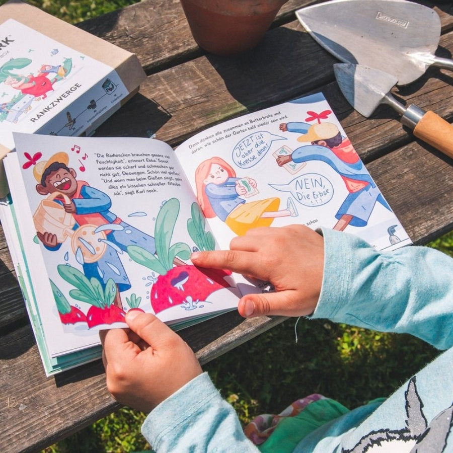Kind guckt sich das Kinderbuch der Rankwerk Saatgut Box Rankzwerge an