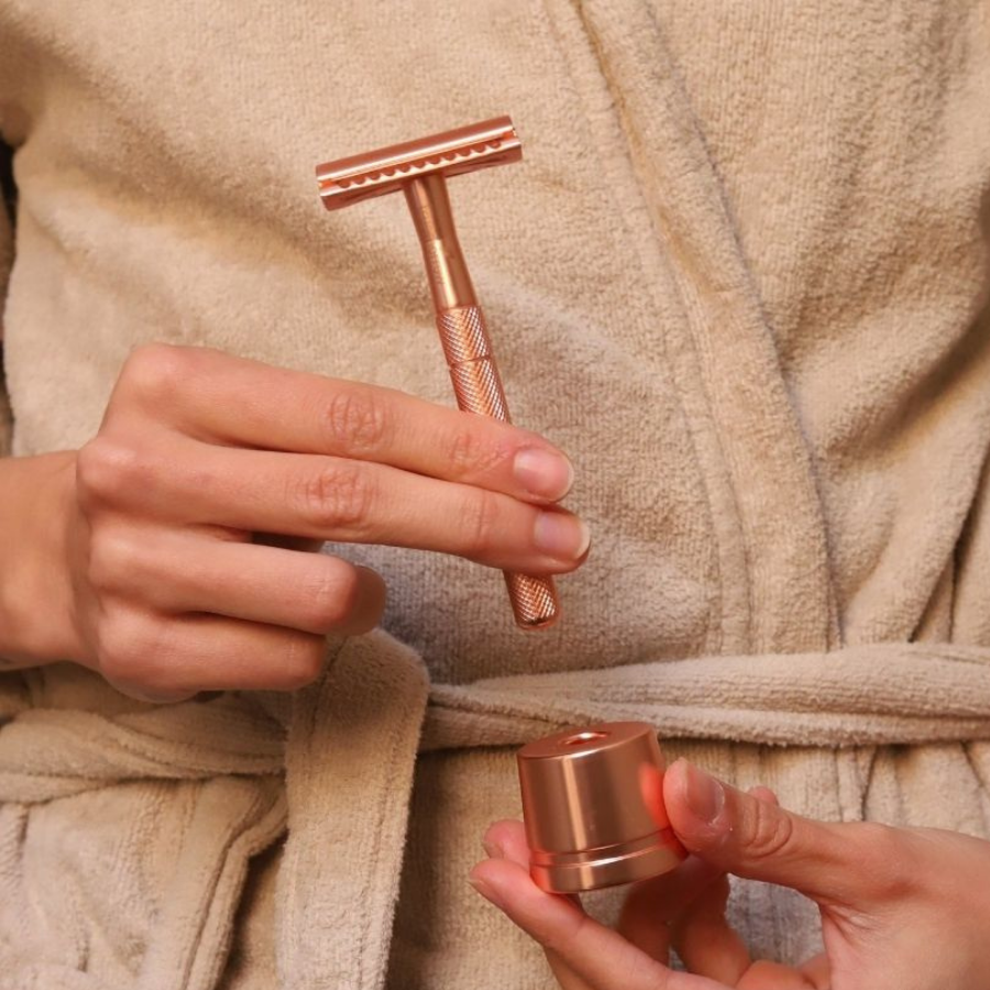 Person mit Bademantel hält den Truemorrow Rasierhobel und Ständer in rose in der Hand