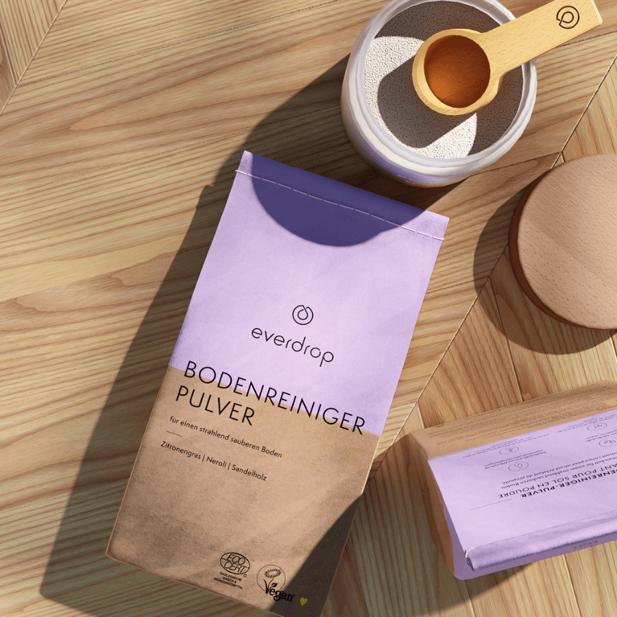 2 Verpackungen everdrop Bodenreiniger Pulver - eine liegend, eine stehend, mit Dosierlöffel im Hintergrund