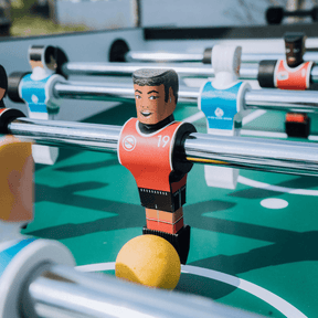 Diverse Tischkicker Figuren, einschließlich Frauen und Männer, auf einem Tischfußballspiel mit buntem Ball.