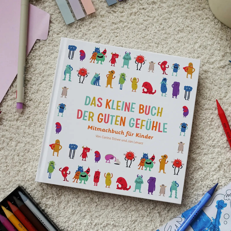 Das kleine Buch der guten Gefühle auf einem Teppich mit Stiften