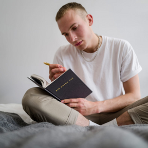 Person sitzt im Schneidersitz und schreibt in das Tagebuch