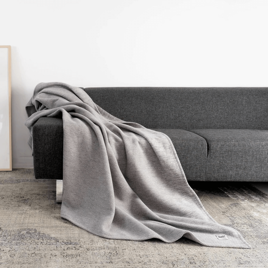 Kushel Decke Woven Silver liegt auf einem grauen Sofa