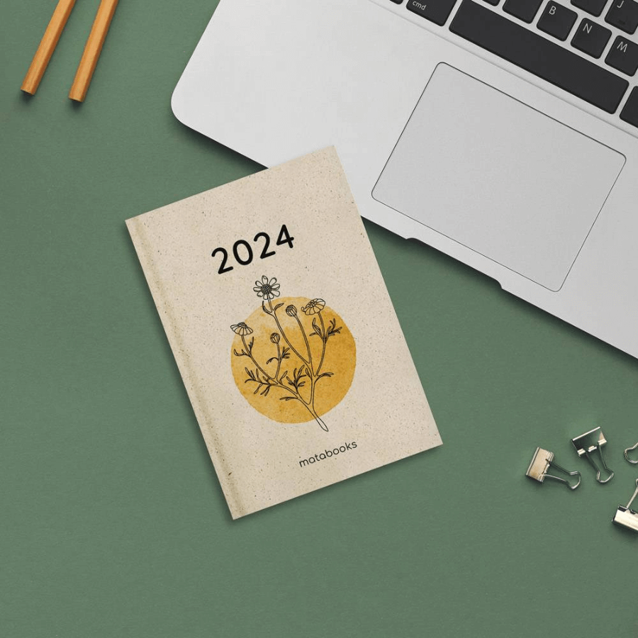 Matabooks Jahresplan Samaya 2024 "Yellow" liegt auf einem Tisch, daneben ein Laptop