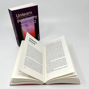 Unlearn Patriarchy 2 geöffnet, im Hintergrund steht ein weiteres Buch