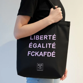 Person trägt Tote Bag – LIBERTÉ ÉGALITÉ FUCK AFD von arrel Schwarz mit hell-lila Schrift 