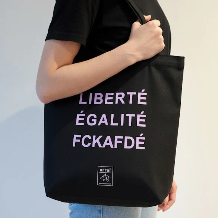 Person trägt Tote Bag – LIBERTÉ ÉGALITÉ FUCK AFD von arrel Schwarz mit hell-lila Schrift 