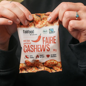 Person reißt fairfood – Cashews mit Chili 50 g Tütchen  auf