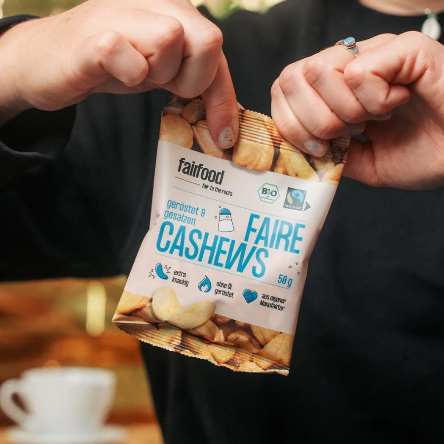 Person reißt fairfood – Cashews gesalzen 50 g Tütchen auf