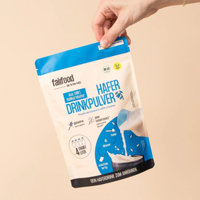 Eine Hand hält den fairfood Haferdrinkpulver im 360g Beutel