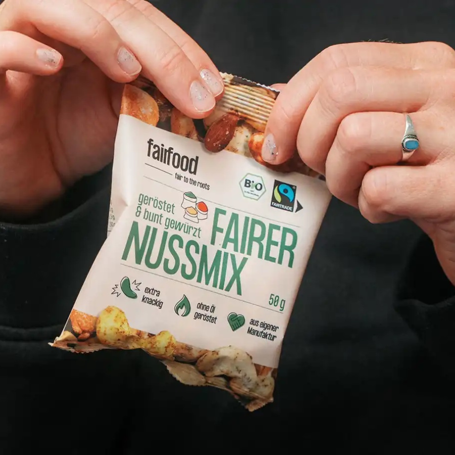 Person reißt fairfood – Fairer Nussmix 50 g Tütchen  auf
