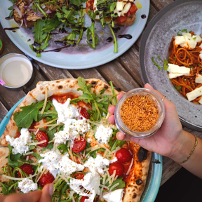 Person streut Gewürzmischung – Chilisalz von SOCHILIüber Pizza