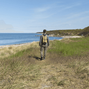 Person trägt Backpack Mini Brown Dark Yellow auf dem Rücken und läuft durch die Natur