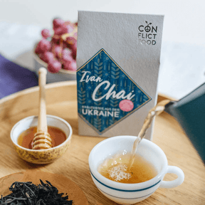Tee wird in eine Tasse eingegossen, im Hintergrund steht Ivan Chai von Conflictfood Verpackung und ein Schälchen mit Honig