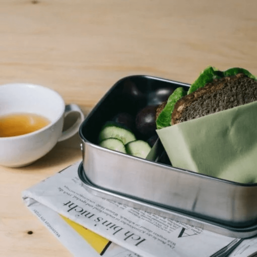 Brotdose von GAIA gefüllt mit Brot, Obst und Gemüse neben einer Tasse Tee