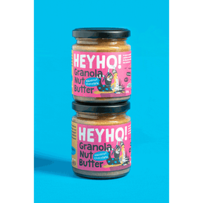 Zwei Gläser Heyho Granola Nussbutter Hazelnut Chocolate stehen übereinander vor blauem Hintergrund