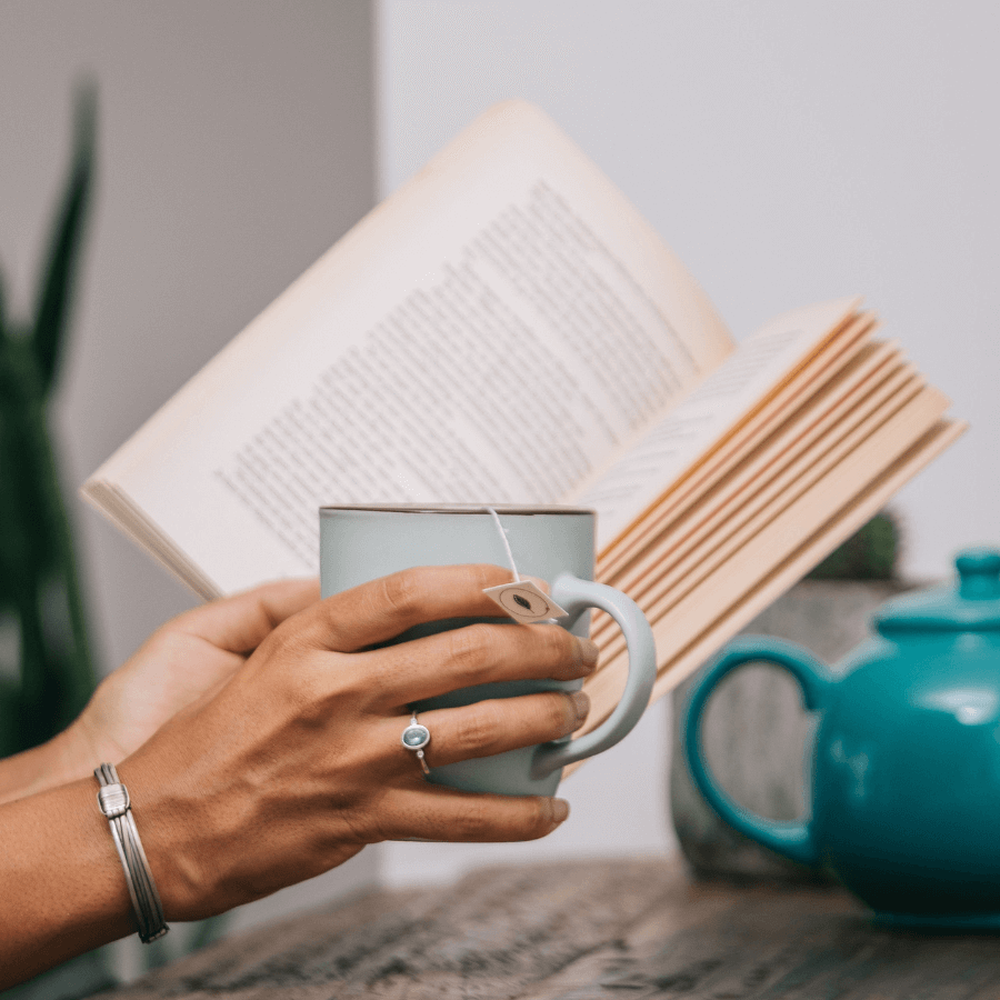 Frau hält Tasse Tee in der Hand und liest ein Buch
