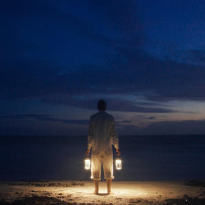 Mann am Strand bei Nacht, der zwei Sonnengläser in den Händen hält.