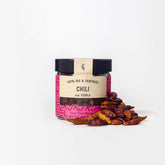 Ganze Chilis in Glasverpackung mit Gewürzhäufchen von vorne 