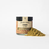 Cumin in Glasverpackung mit Gewürzhäufchen von vorne 