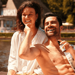 Zwei Personen sitzen lachend in der Sonne und halten die Sonnencreme von truemorrow in der Hand