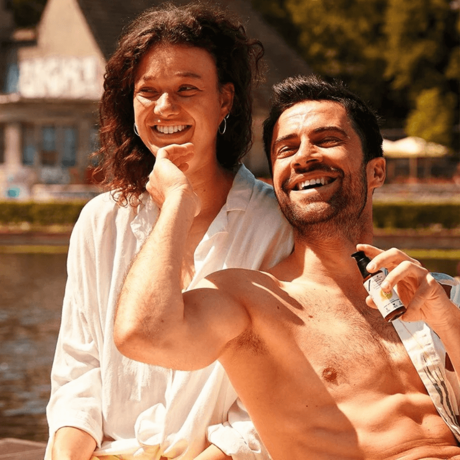 Zwei Personen sitzen lachend in der Sonne und halten die Sonnencreme von truemorrow in der Hand